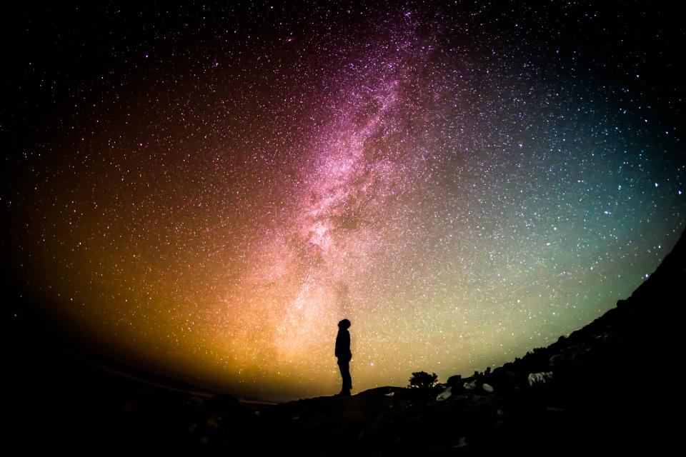 Shadowy figure of a person looking up, galaxy in the background